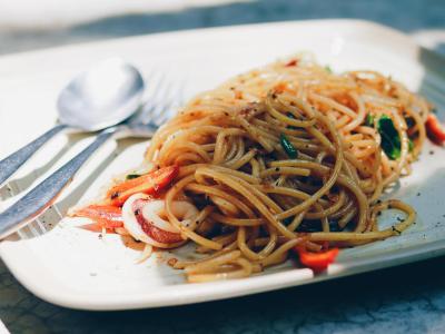 Spaghetti con verdure su piatto quadrato, posate accanto.